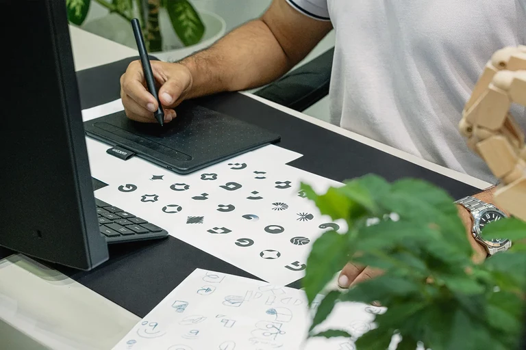 Designer travaillant sur une identité de marque à la tablette graphique, avec des recherches de logos sur le bureau