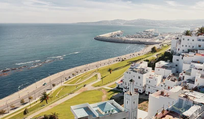 View over Tangier with the sea, port, coastal road, white buildings and a minaret.